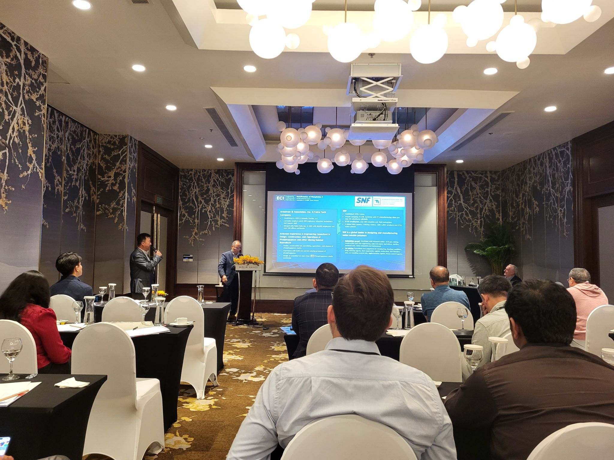 Conference room with attendees watching two speakers present slides about mining and phosphate innovation during an industry event.